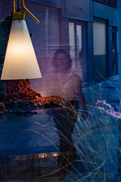 A Nimes une femme marchant dans la rue se reflète dans une vitrine abritant un décor de bord de mer.